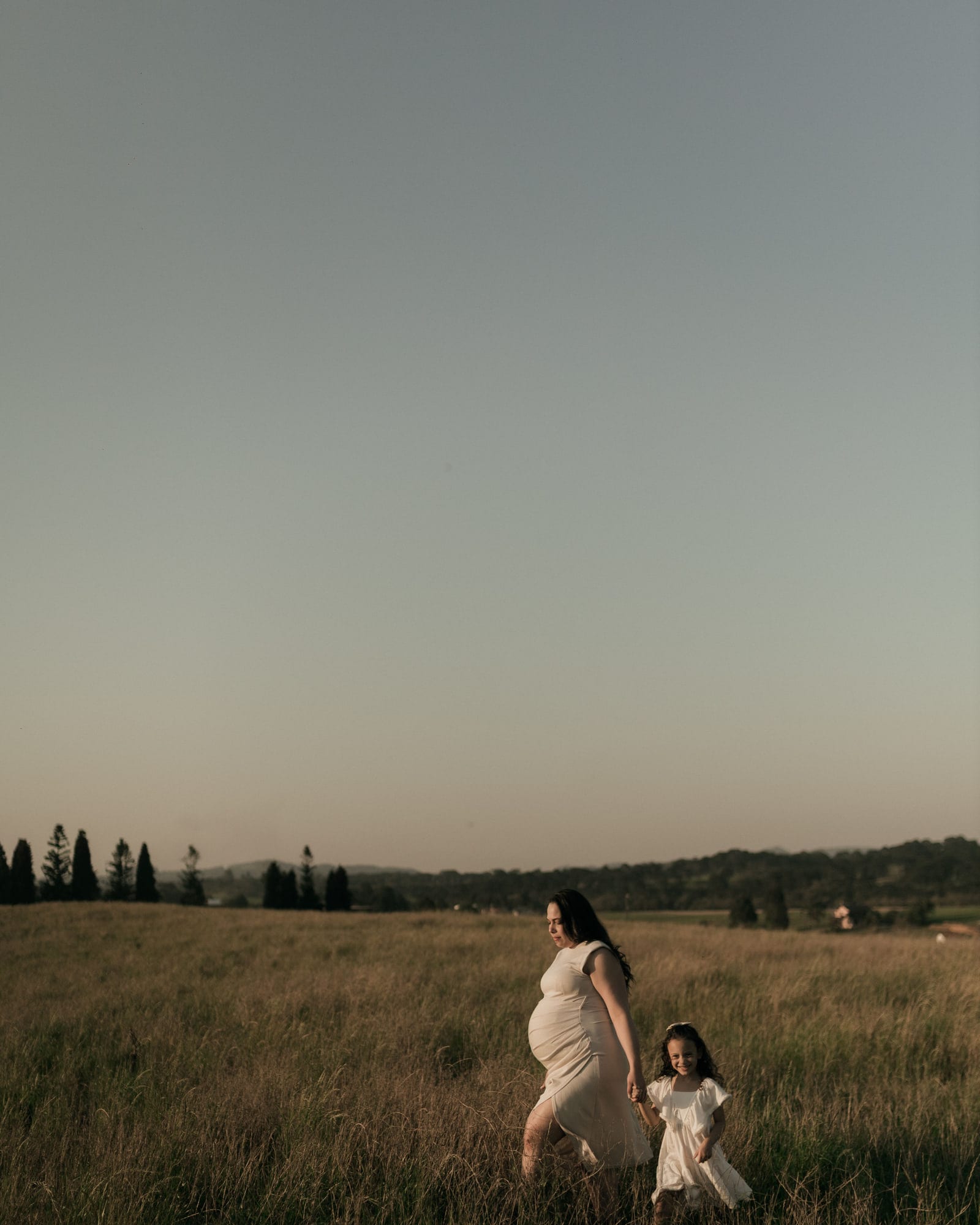 A mother and daughter walking together through a meadow at dusk