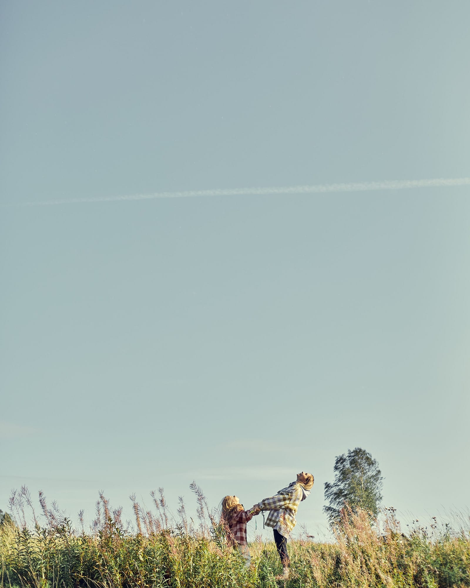 A parent and child walking hand in hand through a field under open sky