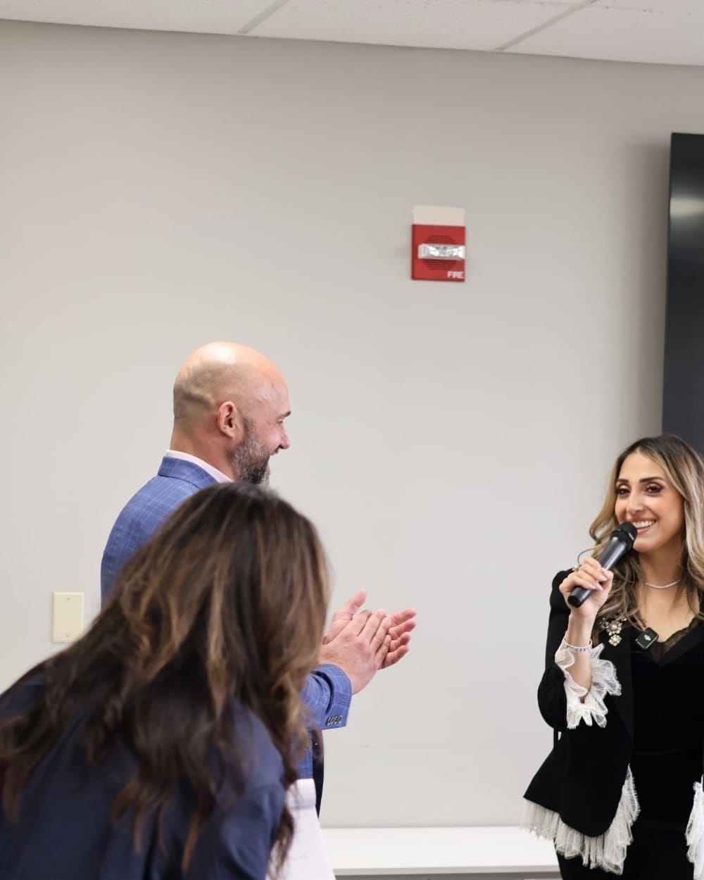 Members of the Synergy team applauding a colleague speaking into a microphone.