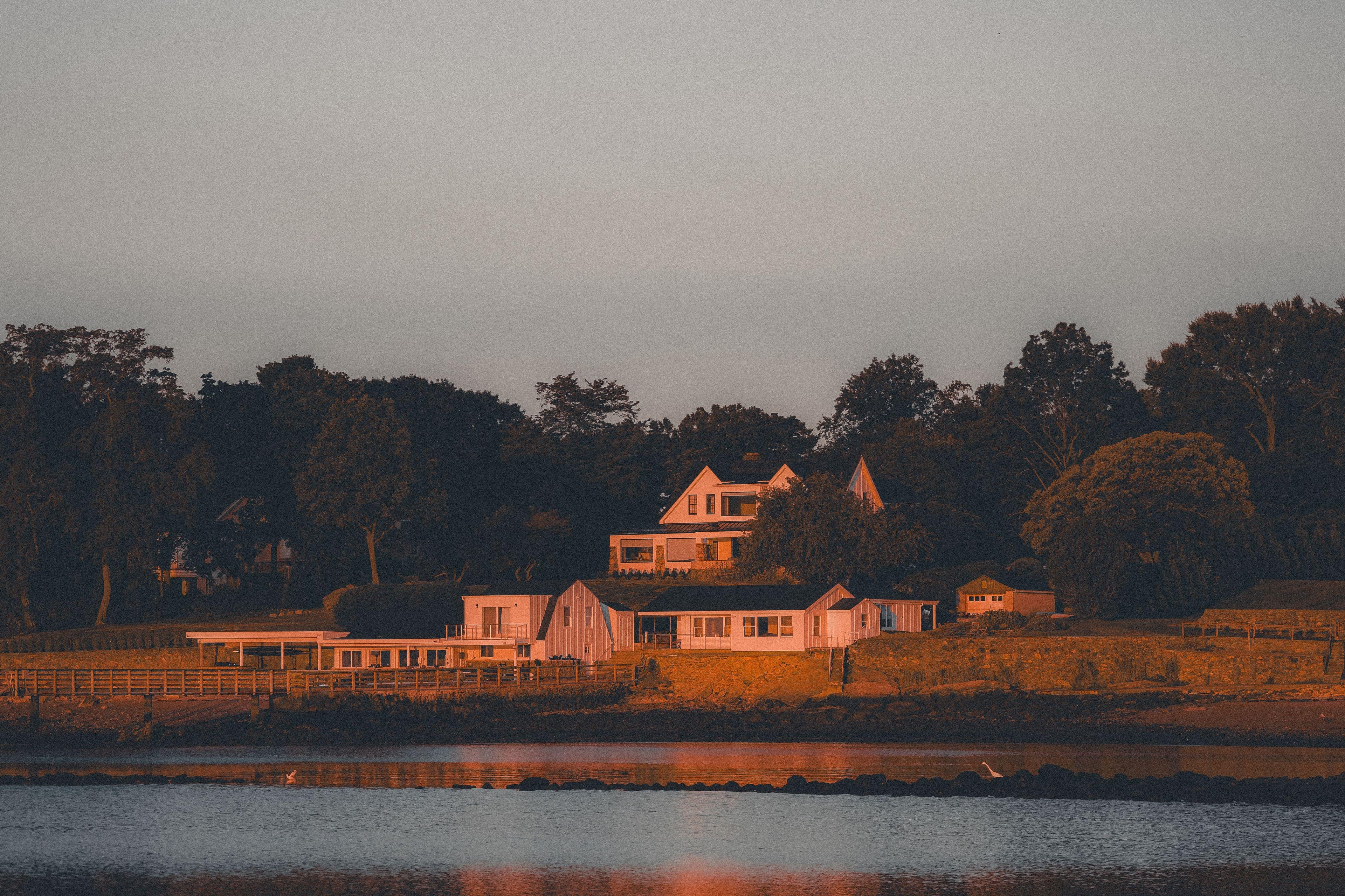 Waterfront homes at dusk with their lights on, seen across calm water.