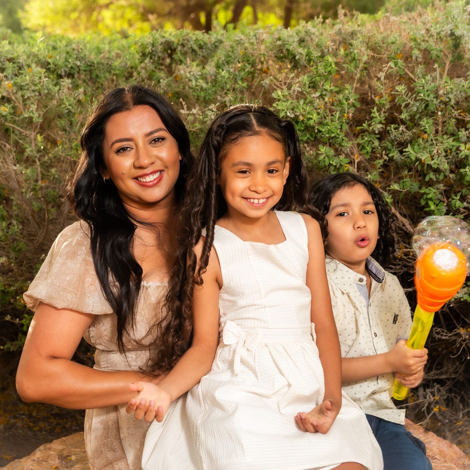 A mother outdoors in late afternoon light with her two young children.